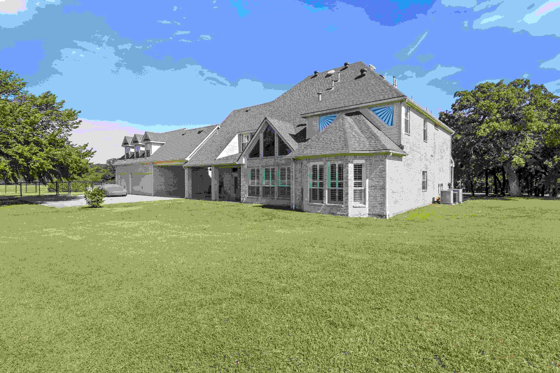 Rear elevation framed by mature oak trees with vaulted living room windows