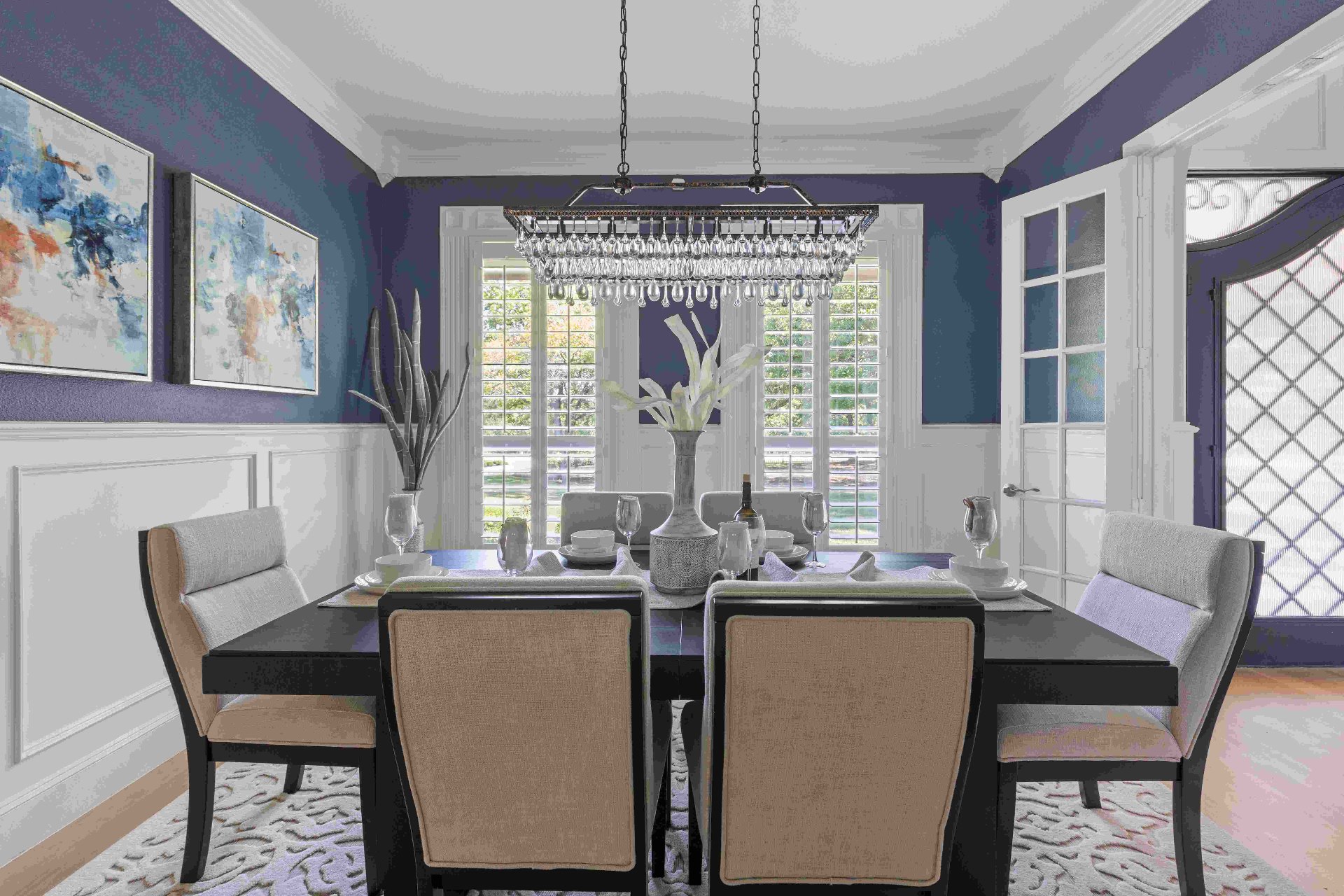 Formal dining room with navy walls, wainscoting, crystal chandelier, and plantation shutters