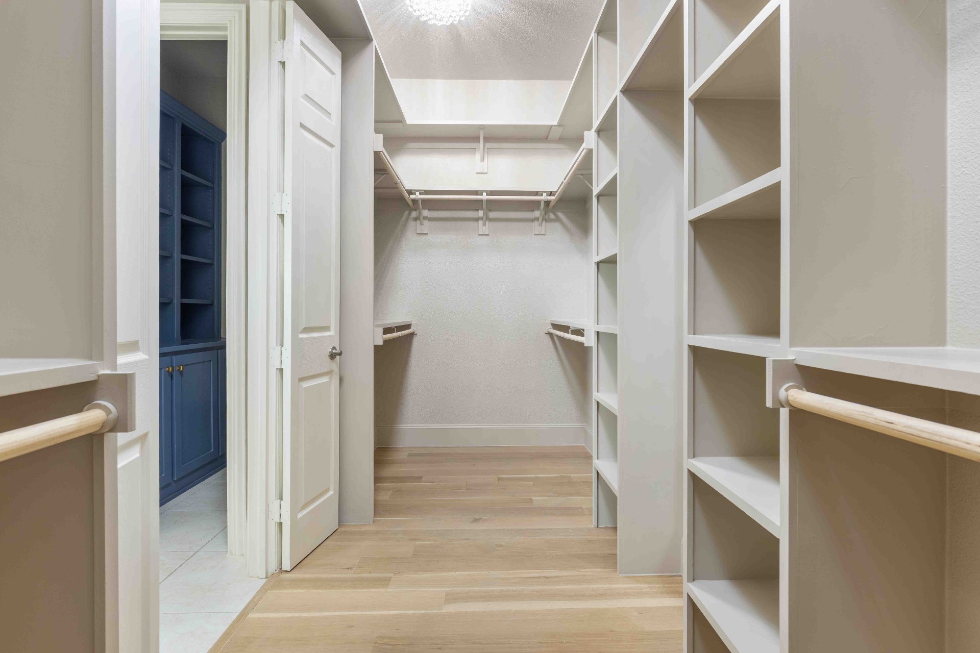 Primary walk-in closet with custom built-in shelving and hardwood floors