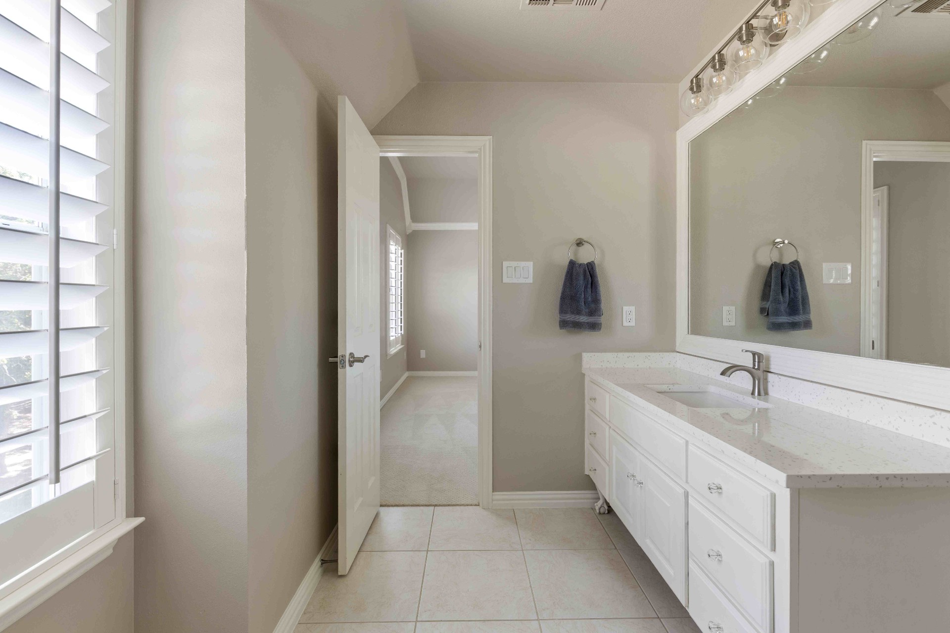 Upstairs bath with white cabinetry, quartz counter, and plantation shutters
