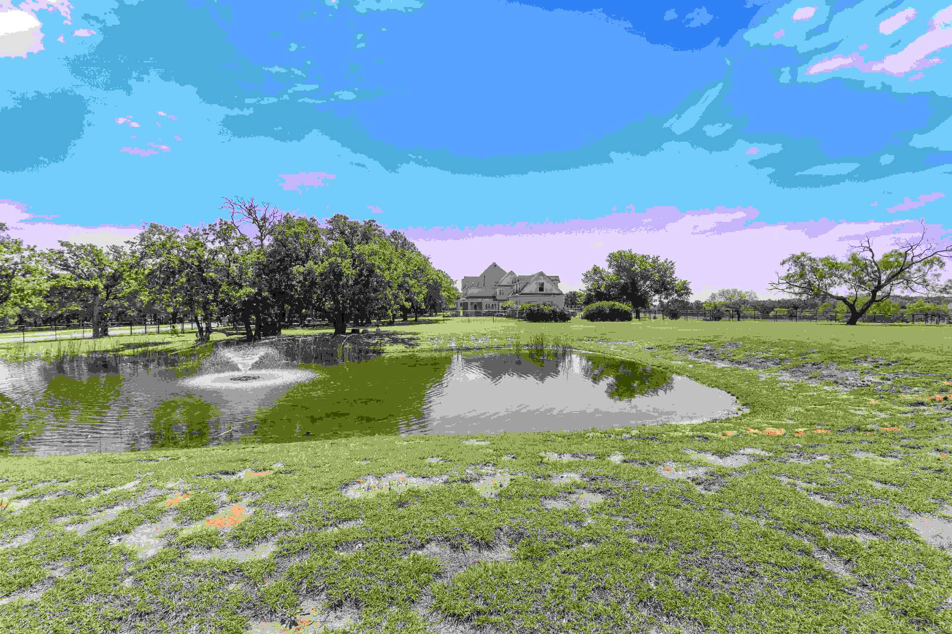 Pond with fountain and the estate home in the background across the open lot